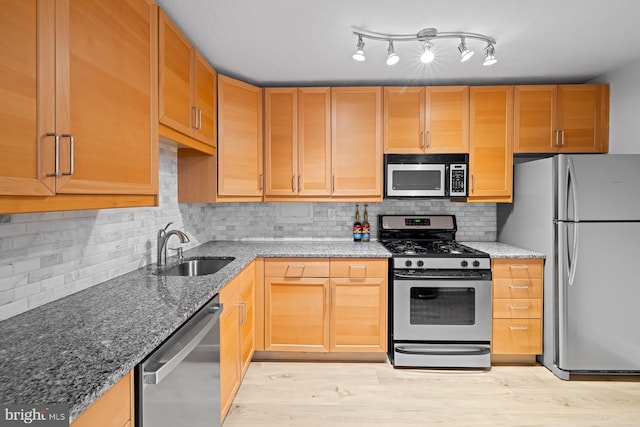 kitchen featuring stainless steel appliances, a sink, stone countertops, and decorative backsplash