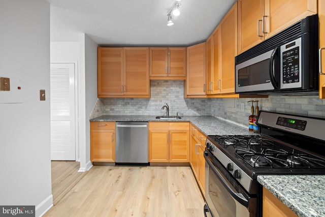 kitchen with appliances with stainless steel finishes, a sink, light wood-type flooring, light stone counters, and tasteful backsplash