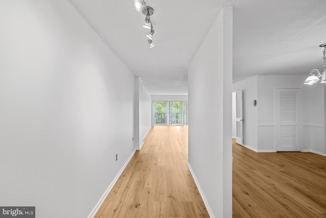 hall with light wood-type flooring, a chandelier, and baseboards