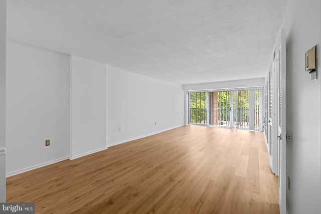 empty room featuring light wood-style flooring, baseboards, and a textured ceiling