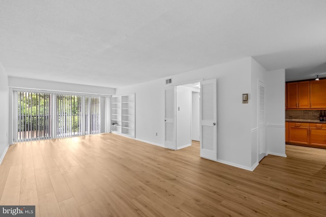 unfurnished living room with baseboards, light wood-style floors, and built in shelves