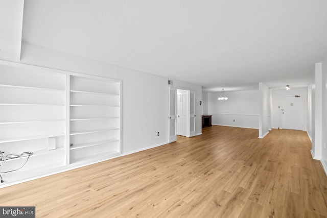 unfurnished living room featuring a chandelier, light wood finished floors, baseboards, and built in shelves