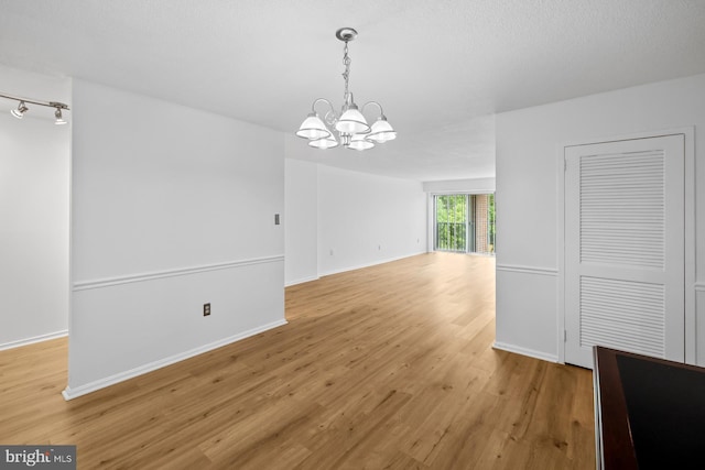 unfurnished dining area with a chandelier, light wood-style floors, rail lighting, and baseboards