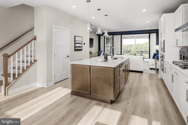 kitchen with light wood-type flooring, a sink, a center island with sink, white cabinets, and light countertops