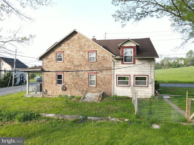 back of house featuring a shingled roof, stone siding, and a chimney