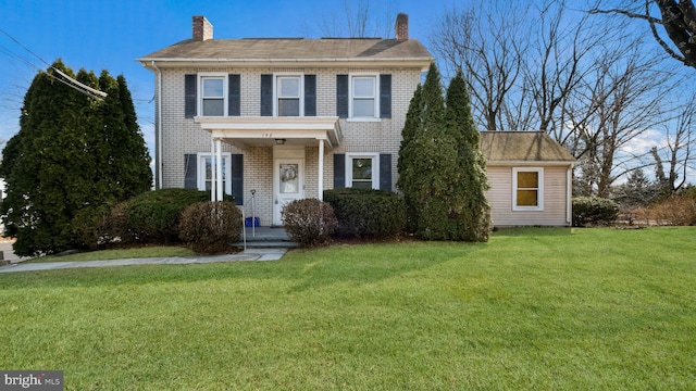 colonial inspired home featuring a chimney, brick siding, and a front lawn