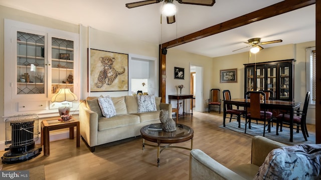 living area with a ceiling fan, wood finished floors, and beamed ceiling