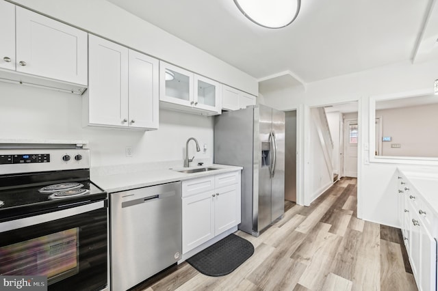 kitchen featuring appliances with stainless steel finishes, a sink, white cabinets, light countertops, and light wood-style flooring
