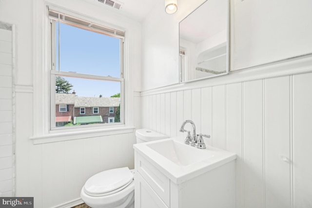 bathroom with a decorative wall, toilet, vanity, and a wainscoted wall