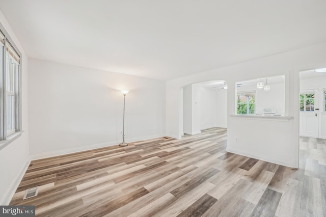 spare room featuring wood finished floors, arched walkways, and baseboards