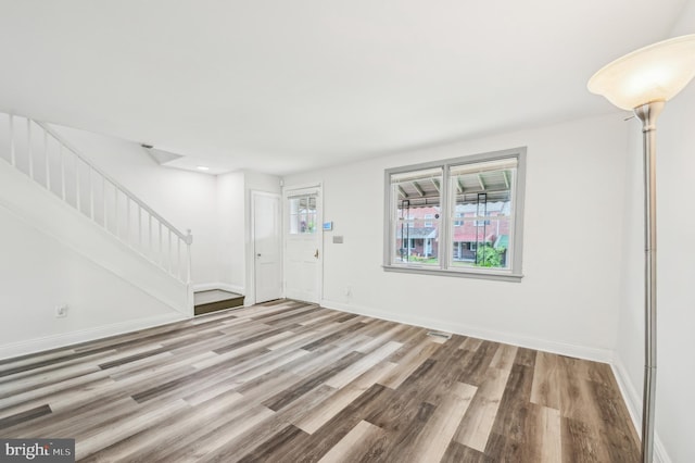 unfurnished living room with stairs, wood finished floors, and baseboards