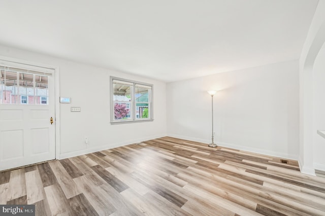 foyer featuring healthy amount of natural light, light wood-type flooring, baseboards, and arched walkways