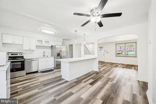 kitchen with appliances with stainless steel finishes, a sink, arched walkways, ceiling fan, and light wood-style floors