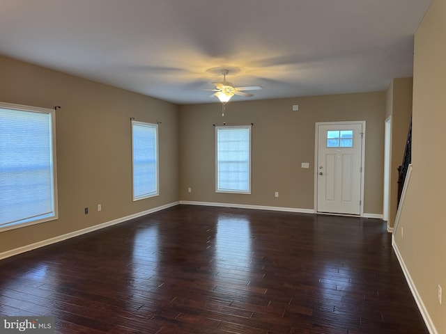 unfurnished living room featuring healthy amount of natural light, dark wood finished floors, ceiling fan, and baseboards