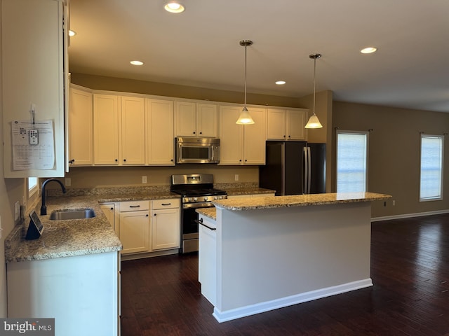 kitchen with appliances with stainless steel finishes, a sink, a kitchen island, dark wood-style floors, and white cabinetry