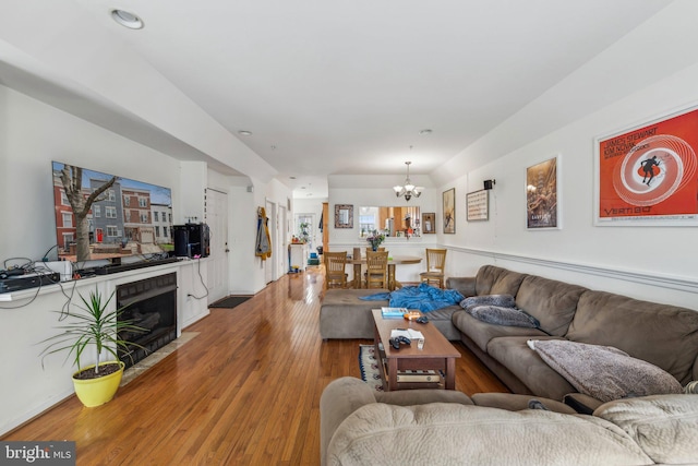 living room with a chandelier, wood finished floors, and a fireplace with flush hearth