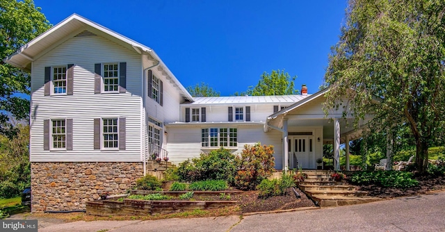view of front of property with a porch, stone siding, metal roof, and a chimney