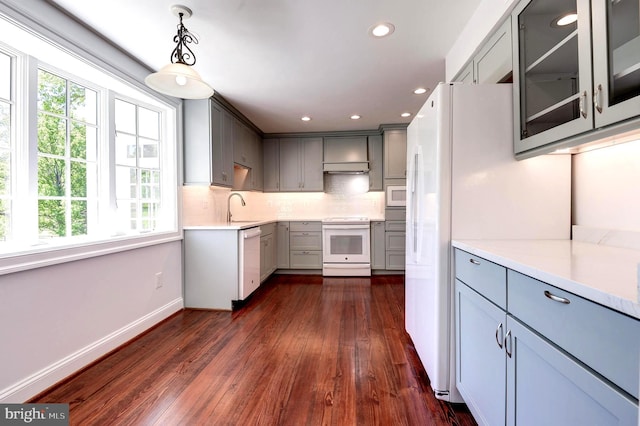 kitchen with white appliances, gray cabinets, a sink, dark wood-style floors, and under cabinet range hood