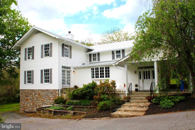 view of front of property featuring a chimney, a porch, stone siding, and metal roof