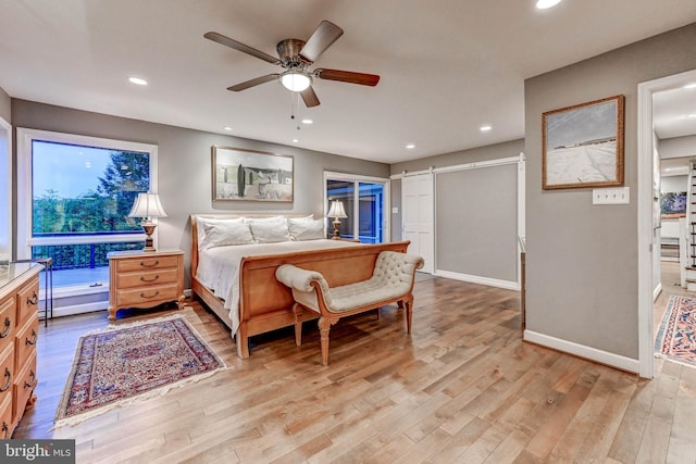 bedroom with light wood-type flooring, baseboards, recessed lighting, a barn door, and a ceiling fan