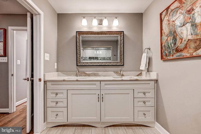 bathroom with double vanity, baseboards, and wood finished floors