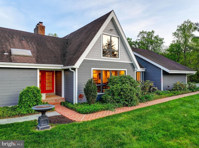 view of front of home featuring a front yard, a chimney, and a shingled roof