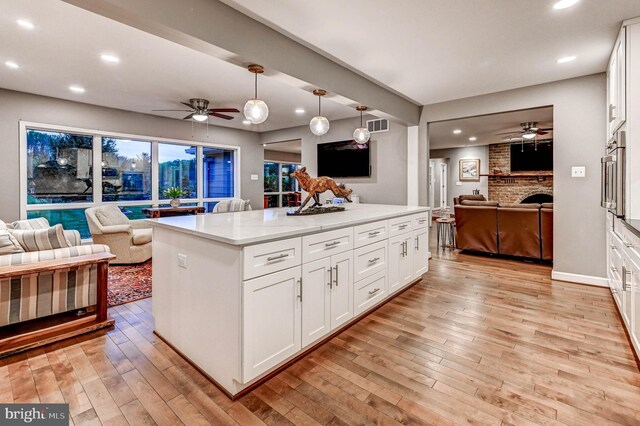 kitchen with open floor plan, a ceiling fan, a fireplace, light wood-style floors, and recessed lighting