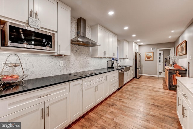 kitchen featuring wall chimney exhaust hood, stainless steel appliances, light wood finished floors, decorative backsplash, and recessed lighting