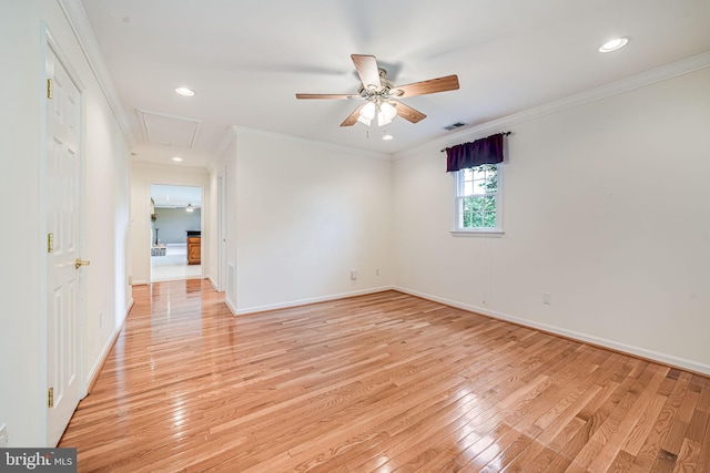 empty room featuring attic access, light wood-type flooring, a ceiling fan, baseboards, and crown molding