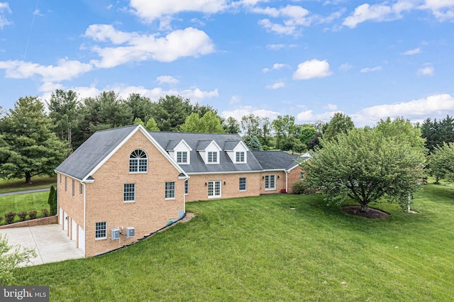rear view of property featuring concrete driveway, brick siding, an attached garage, a yard, and view of scattered trees