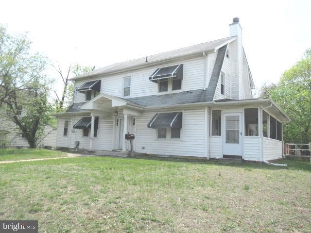 rear view of house featuring a chimney, a sunroom, and a lawn