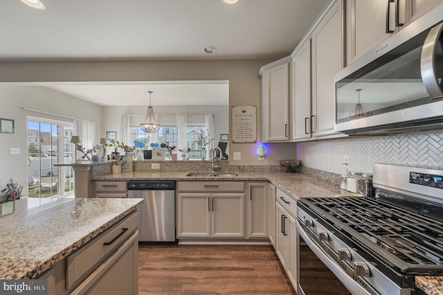 kitchen featuring appliances with stainless steel finishes, a sink, a peninsula, light stone countertops, and recessed lighting