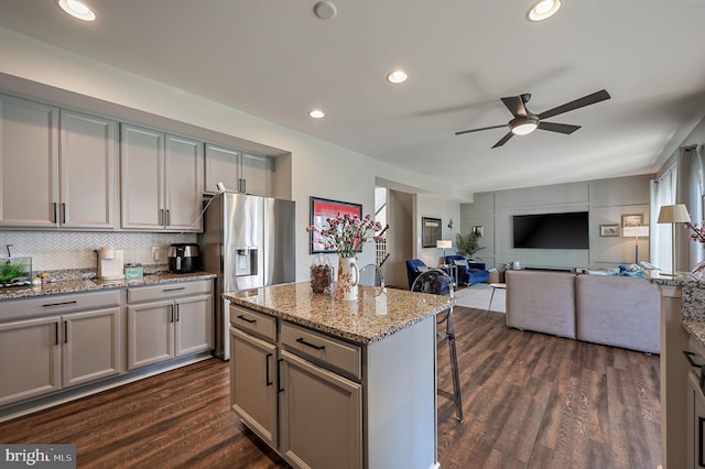kitchen featuring stainless steel fridge, gray cabinets, a ceiling fan, a kitchen breakfast bar, and dark wood-style floors