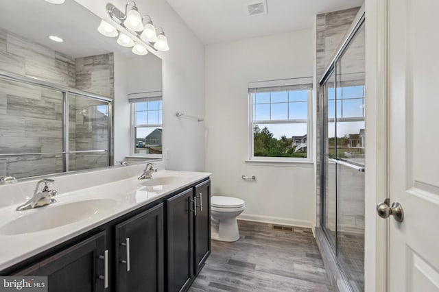 bathroom with a shower stall, double vanity, wood finished floors, and baseboards