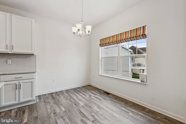 unfurnished dining area featuring wood finished floors, a chandelier, and baseboards