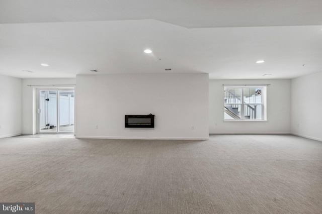 unfurnished living room with light carpet, a glass covered fireplace, recessed lighting, and baseboards