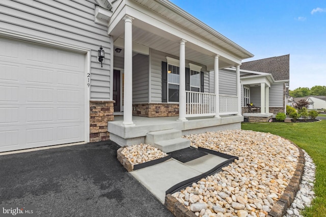 view of exterior entry with covered porch, stone siding, an attached garage, and a shingled roof
