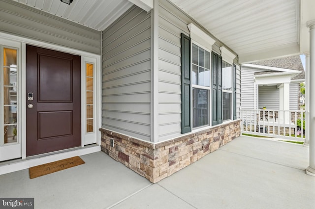 view of exterior entry featuring covered porch and stone siding