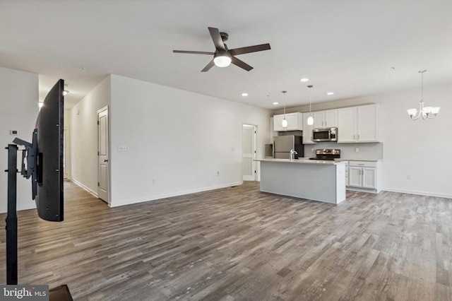 unfurnished living room with ceiling fan, a chandelier, wood finished floors, recessed lighting, and baseboards