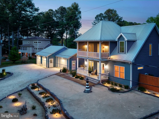 view of front facade with a porch, driveway, a balcony, an outbuilding, and metal roof