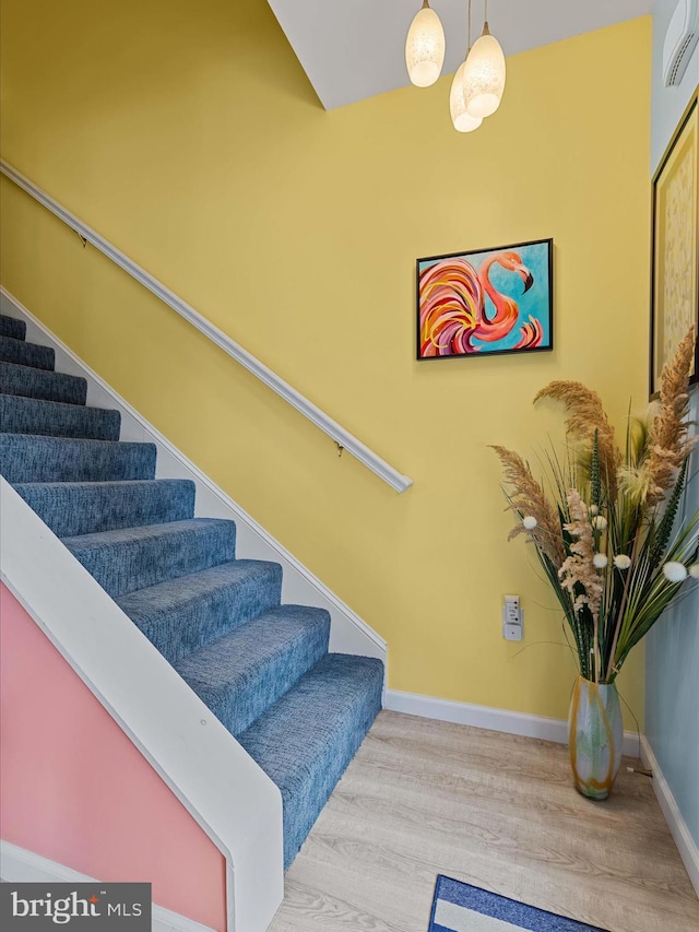stairs with wood finished floors, baseboards, and a wall unit AC