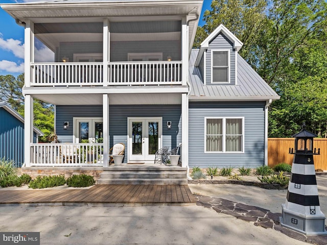 back of property with french doors, a balcony, covered porch, and fence