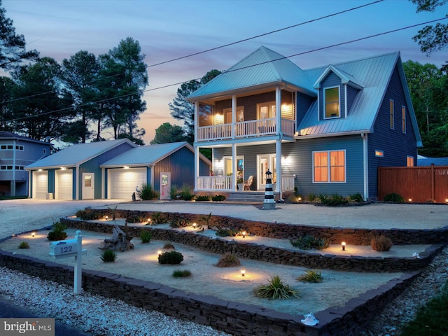 rear view of house featuring a porch, a balcony, concrete driveway, metal roof, and fence