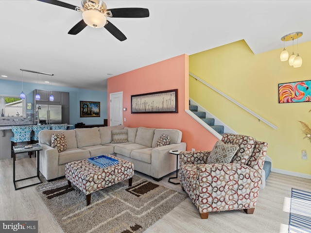 living area with wood finished floors, a ceiling fan, and stairway