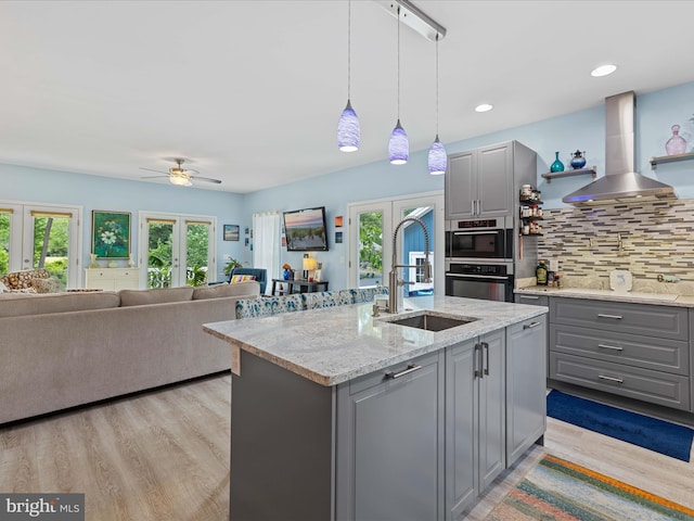 kitchen with gray cabinetry, a sink, wall chimney range hood, french doors, and recessed lighting