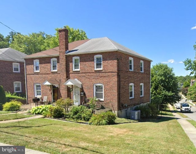 colonial house with a chimney, central AC unit, a front yard, and brick siding