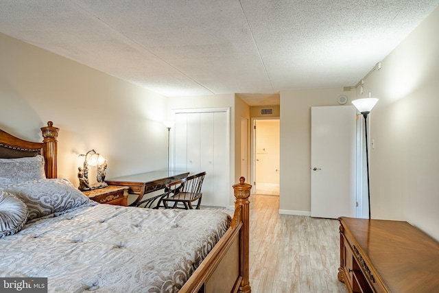 bedroom featuring light wood-style flooring, a textured ceiling, a closet, and baseboards