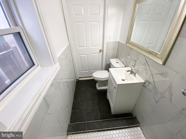 bathroom with toilet, vanity, wainscoting, and tile walls