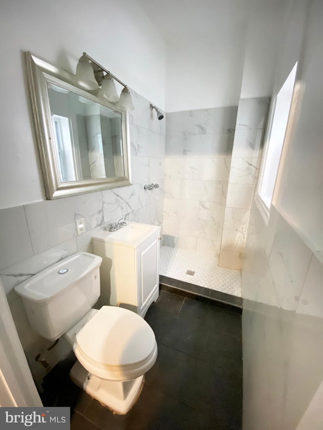 full bath with tiled shower, tile walls, toilet, and vanity