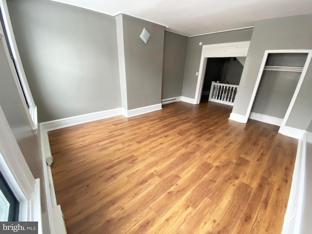 empty room featuring wood finished floors, baseboard heating, and baseboards